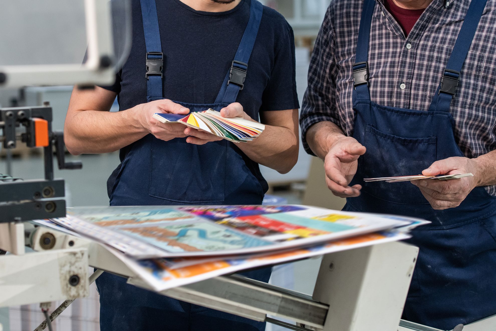 I professionisti della stampa ispezionano attentamente brochure e materiali di marketing di alta qualità durante la produzione. Questa immagine mostra il controllo qualità e l'artigianalità professionale dietro i servizi di stampa economica che offrono risultati vibranti e accattivanti. Ideale per le aziende che cercano soluzioni stampate convenienti senza sacrificare la qualità visiva o le finit…