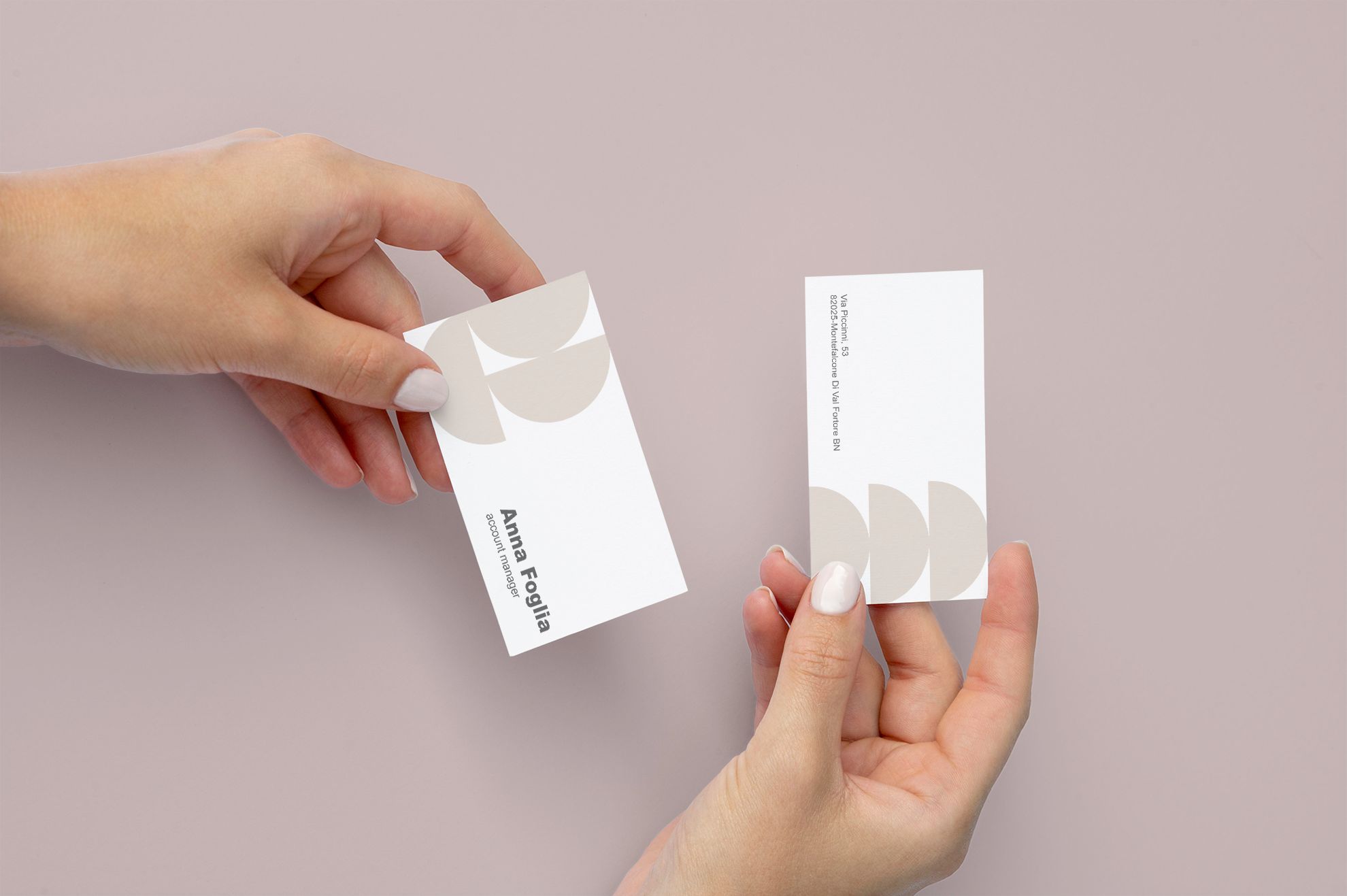 Due mani che si scambiano biglietti da visita in formato verticale con design minimale beige e bianco con forme a semicerchio astratte su sfondo malva. I biglietti da visita in formato verticale sono ideali per designer, architetti e creativi che desiderano un'identità stampata distintiva ed elegante — disponibili con varie grammature di carta e finiture opzionali.