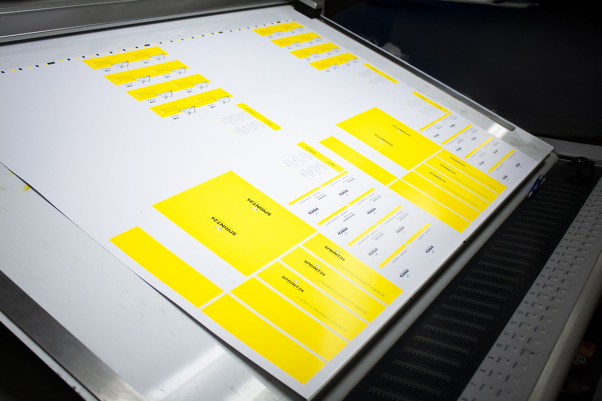 Un foglio di stampa in grande formato con blocchi di calibrazione gialli su una macchina da stampa digitale professionale di Sprint24. Questa immagine rappresenta il processo di stampa offset e digitale di alta qualità al centro dei servizi di tipografia online di Sprint24. Le nostre macchine all'avanguardia garantiscono precisione cromatica e risultati costanti per tutti i prodotti stampati.