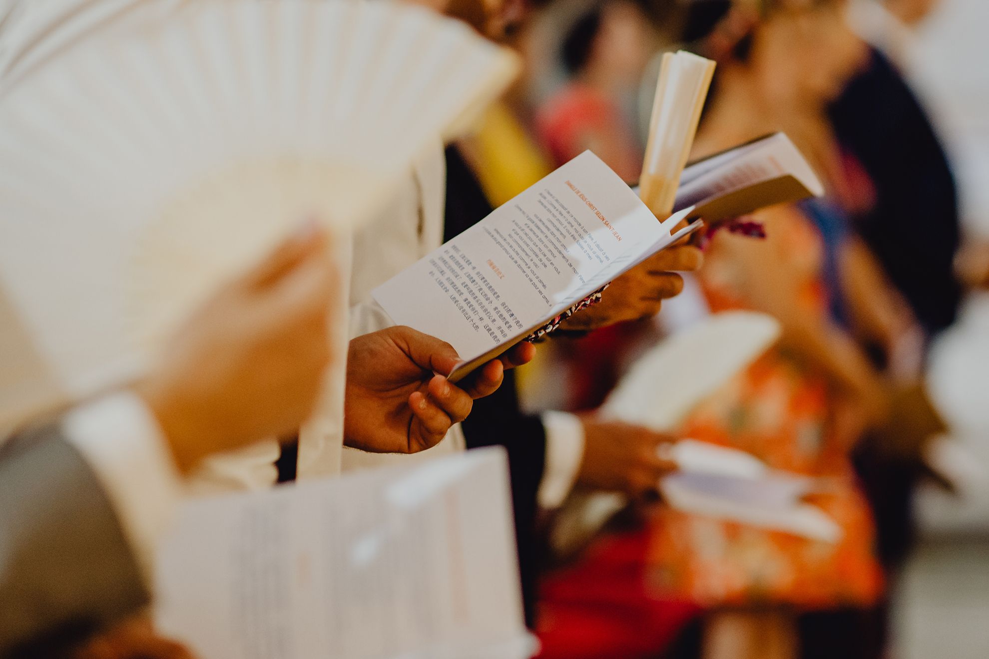 Una mano che tiene aperto il libretto di matrimonio durante la cerimonia. I libretti di matrimonio aiutano gli invitati a seguire l'ordine della cerimonia, le letture e i momenti importanti con maggiore attenzione. Questo elegante prodotto stampato è un elemento essenziale della pianificazione e del design della cerimonia di matrimonio.