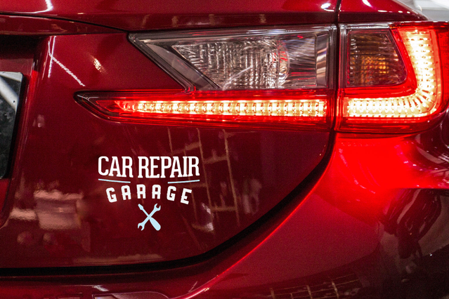 Adesivo prespaziato bianco 'Car Repair Garage' applicato sul posteriore di un'auto rossa accanto al fanale. Sprint24 stampa adesivi prespaziati personalizzati su vinile lucido bianco con durata fino a 60 mesi — ideali per branding veicoli, vetrine e cartellonistica con applicazione a secco senza bolle.