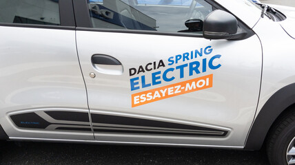 Adesivo commerciale professionale applicato a un veicolo elettrico Dacia Spring bianco, che dimostra messaggi promozionali personalizzati per il branding aziendale della flotta. Gli adesivi auto aziendali come questi offrono pubblicità ad alta visibilità sui veicoli, perfetti per campagne aziendali e visibilità promozionale automobilistica. I decalcomanie personalizzati garantiscono stampa di qua…