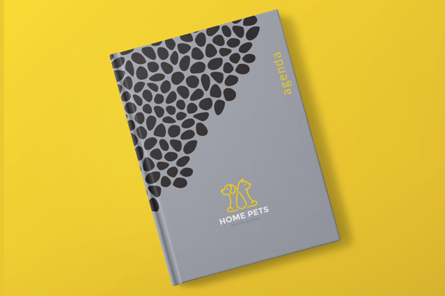 Un'agenda cartonata settimanale chiusa grigia con motivo ciottoli organici neri nell'angolo superiore e logo giallo 'Home Pets' cane e gatto, su vivace sfondo giallo. Ideale per pet shop, aziende e professionisti che cercano agende cartonate settimanali personalizzate (1 settimana su 2 pagine, 128 pagine, 3 impaginati personalizzabili) che combinano pianificazione settimanale pratica con forte id…
