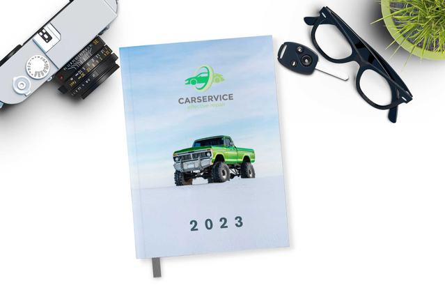 Un'agenda filorefe giornaliera 2023 'CarService' con copertina foto realistica camion verde rialzato su sfondo salina bianca, su scrivania bianca con occhiali, macchina fotografica e chiavi auto. Ideale per officine, autoservizi e professionisti del settore automotive che cercano agende filorefe giornaliere personalizzate (1 giorno per pagina, 336 pagine, carta Fedrigoni) con copertina fotografic…