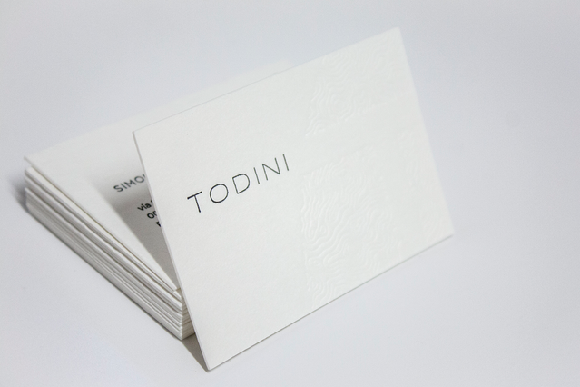 Biglietti letterpress bianchi in carta cotone con lettere in bassorilievo, che mostrano la tecnica elegante di scavo a secco su carta premium da 600g. Il rilievo dimensionale visibile crea un'impressione di lusso sofisticata e tattile, ideale per biglietti da visita professionali e cancelleria di lusso.