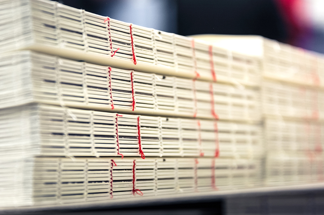 Più pile di blocchi libro con filo refe rosso visibile sul dorso, fotografati in ambiente di produzione tipografica. Sprint24 è specializzata nella rilegatura in filo refe con dorso scoperto per edizioni di pregio, cataloghi e pubblicazioni uniche — una tecnica artigianale che trasforma la rilegatura stessa in elemento di design.