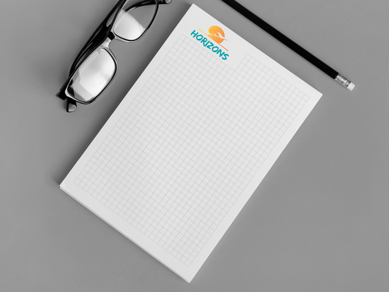 Un block notes A4 personalizzato con template a quadretti fini e logo Horizons in cima, con occhiali e matita su scrivania grigia. I block notes A4 personalizzati con template stampati — millimetrato, puntinato, a quadretti o a righe — sono pratici strumenti promozionali apprezzati per aziende e professionisti che desiderano distribuire un oggetto di cancelleria brandizzato.
