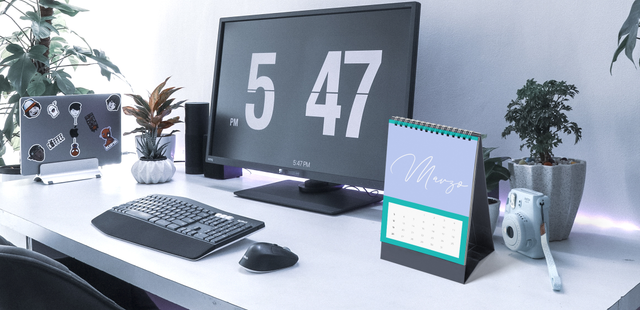 Calendario da tavolo a spirale con copertina personalizzata, appoggiato su una scrivania moderna accanto a tastiera, monitor e piante. Mostra come un piccolo calendario personalizzato trovi spazio su qualsiasi scrivania da ufficio. Perfetto come regalo aziendale sempre sotto gli occhi dei clienti tutto l'anno.
