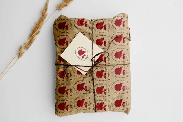 Un pacco avvolto in carta regalo kraft personalizzata stampata con un motivo ripetuto di fragole rosse e legato con spago rustico, completo di piccola etichetta ringraziamento. Sprint24 stampa rotoli di carta regalo personalizzata a colori o B&N con motivi, loghi e nobilitazioni — perfetti per packaging retail, festività e confezioni regalo a tema brand.