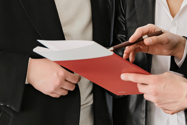 Una cartella portadocumenti personalizzata rossa brillante scambiata tra professionisti in ambiente aziendale, esemplificando come le cartelle di marca migliorano le presentazioni commerciali e le impressioni dei clienti. Le cartelline portadocumenti personalizzabili di Sprint24 offrono tasche e alette per organizzare i documenti mentre mettono in risalto l'identità della vostra azienda durante r…