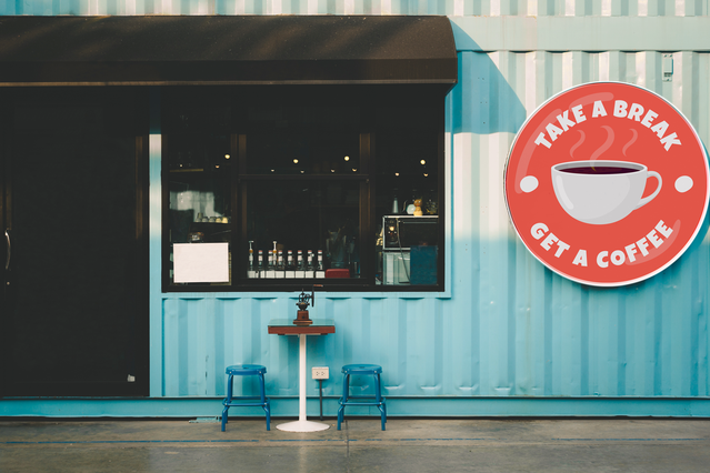 Cartello pubblicitario esterno accattivante con marchio rosso vibrante su una facciata di caffè contemporanea. Questo design di cartello stampato dimostra un posizionamento della segnaletica efficace che attira l'attenzione dei clienti e comunica chiaramente l'identità della tua attività. Ideale per caffè, ristoranti e negozi al dettaglio che cercano una promozione esterna impattante.