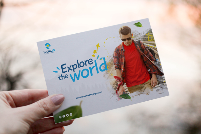 Una mano che tiene una cartolina personalizzata orizzontale per il brand travel 'Walkin' con tipografia audace 'Explore the World', logo e foto a colori di un giovane uomo con occhiali da sole e camicia rossa. Le cartoline personalizzate sono un potente strumento di marketing — ideali per agenzie di viaggio, promozione eventi, campagne coupon e pubblicità direct mail ad alto impatto visivo.