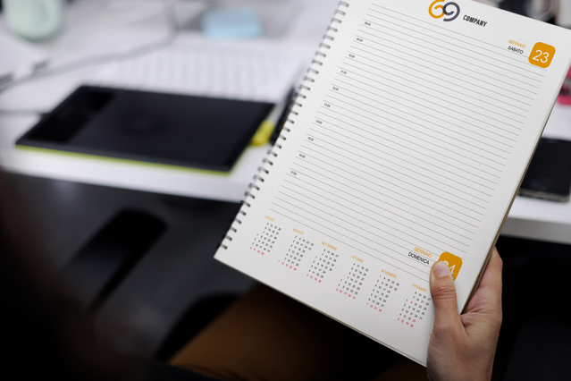 Mano con agenda spirale giornaliera aperta logo G9 arancione timbro data e mini-calendario. Sprint24.