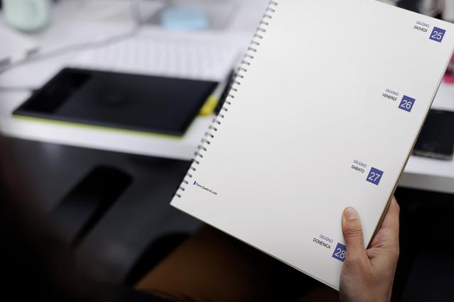 Mano con agenda spirale settimanale aperta doppia pagina timbri data blu. 128 pagine Fedrigoni Sprint24.