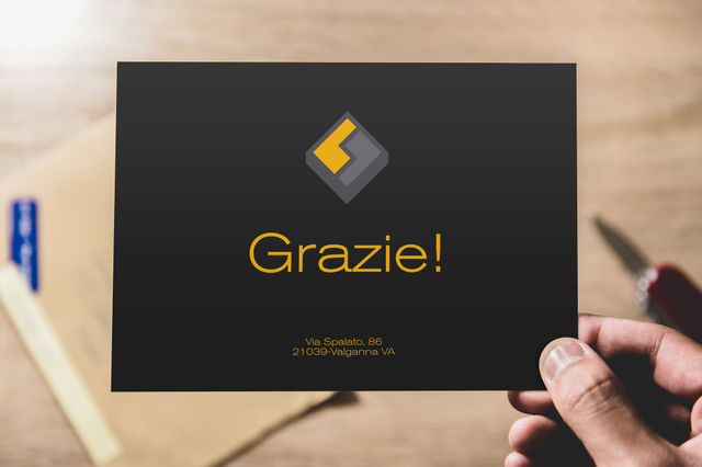Mano con thank you card nera Grazie logo diamante dorato su scrivania legno. Fedrigoni Sprint24.