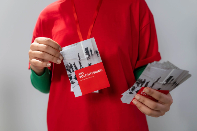 Persona camicia rossa con cartoline promo Art Volunteering rosso bianco per distribuzione. Sprint24.