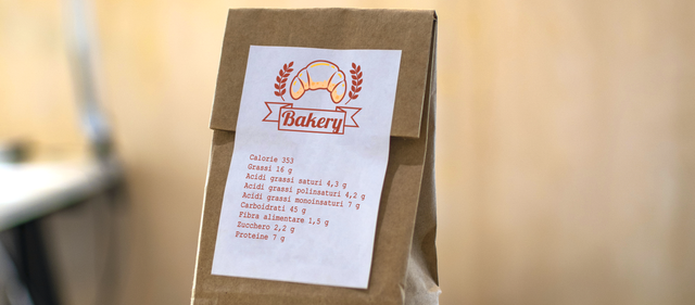 Etichetta adesiva in carta bianca con design panetteria personalizzato su sacchetto kraft. Questo adesivo stampato mostra informazioni prodotto e branding decorativo, ideale per imballaggio alimentare e piccole imprese. Esempio premium di etichette adesive in carta personalizzate.