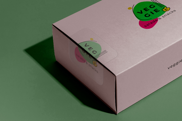Una scatola prodotto rettangolare rosa decorata con adesivo trasparente in PVC 'Veggie' colorato con pallini grafici verdi e rosa. Sprint24 stampa adesivi trasparenti in PVC senza bianco di fondo — perfetti per packaging prodotto, decorazione di brand su superfici colorate e display commerciali.