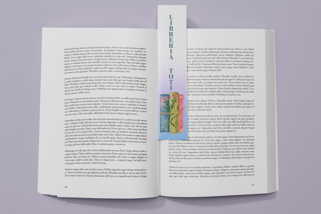 Un libro cartonato aperto con un segnalibro personalizzato lungo e illustrato, decorato con grafica e testo verticale, inserito fra le pagine. Sprint24 stampa segnalibri personalizzati con piena personalizzazione: forma, dimensione, plastificazione e dettagli lucidi — perfetti come gadget promozionali, inserti press kit e omaggi per librerie.