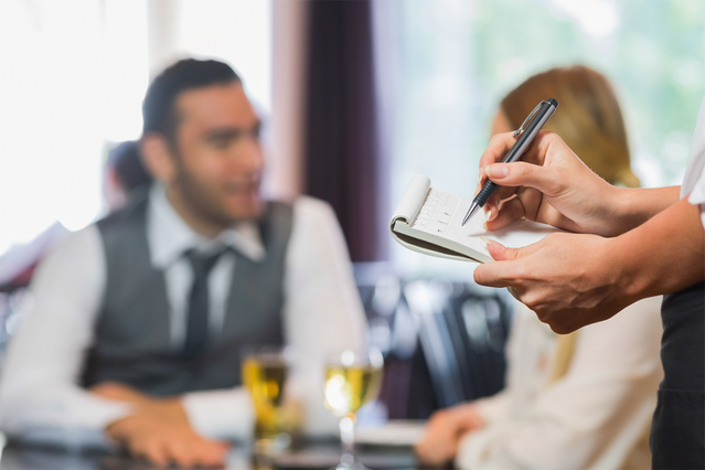 Cameriere che registra una comanda cliente con blocco e penna in un ristorante. I blocchi comande copiativi di Sprint24 semplificano la gestione delle comande con numerazione progressiva e copie multiple per ristoranti, hotel e pub.