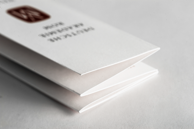 Pieghevoli bianchi stampati professionalmente con logo minimalista marrone, in 2 pantoni su carta kriocolor premium. Con cordonatura precisa e piega a soffietto per una presentazione nitida e professionale. Ideale per stampa depliant di qualità e materiali promozionali.